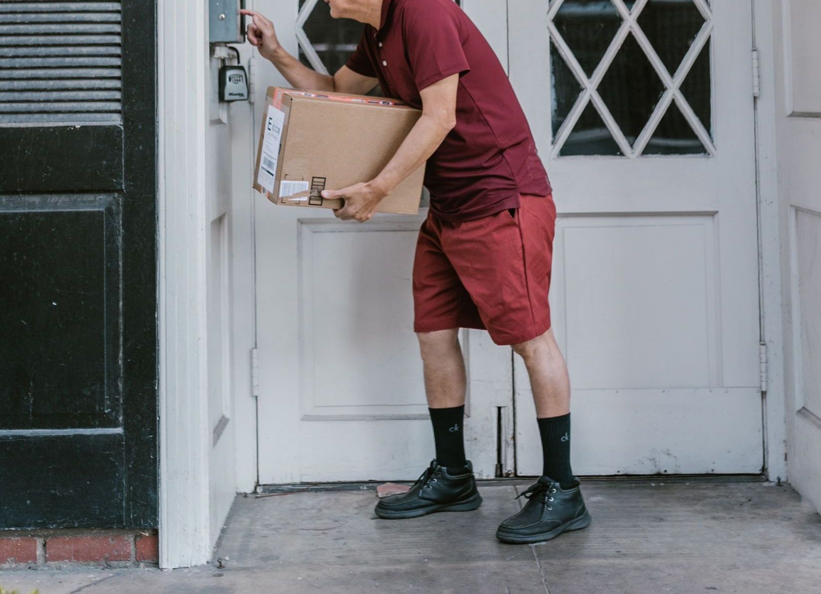 A courier in uniform delivers a package at a residential entrance, ringing the doorbell.
