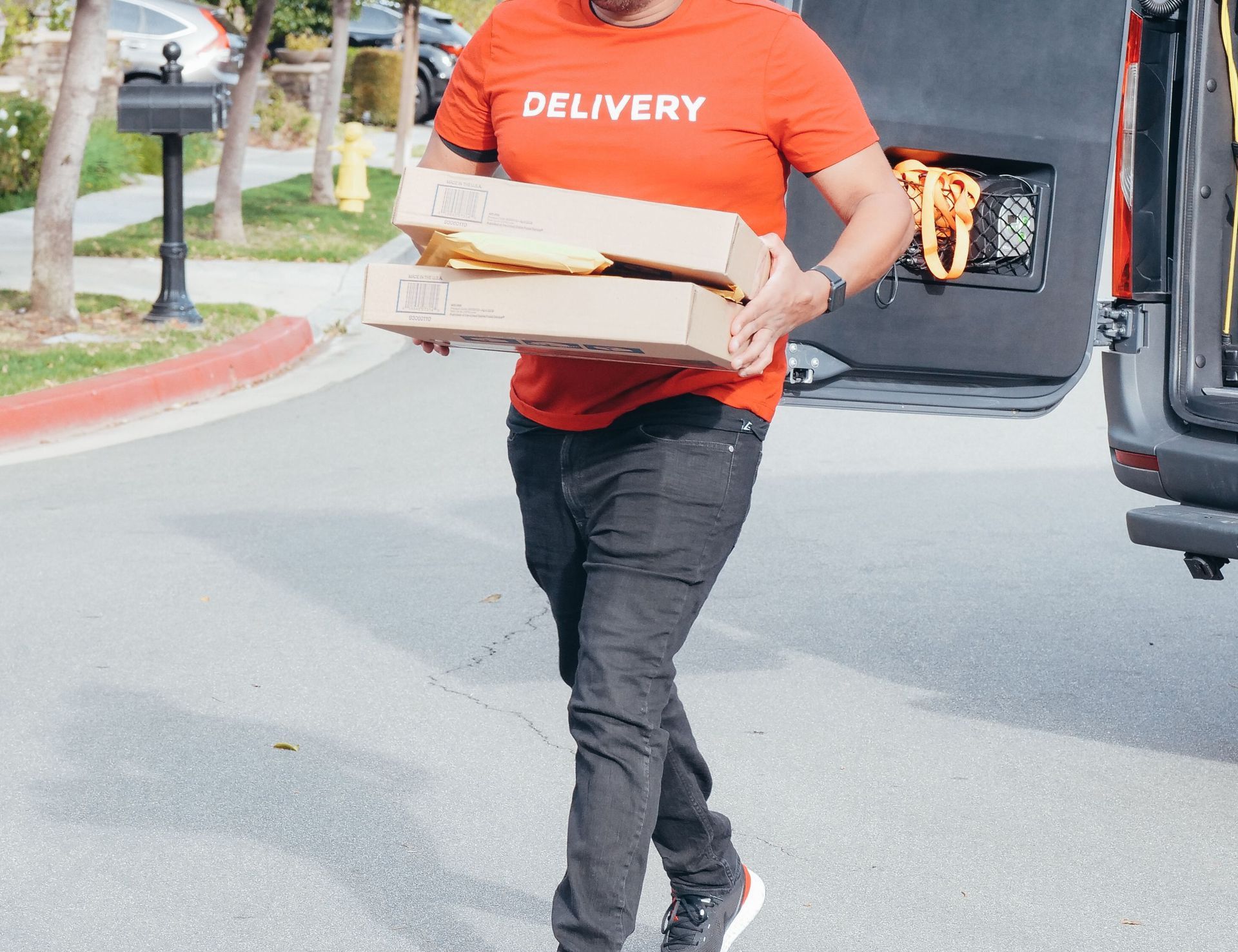 Delivery man in red shirt carrying package from van on a sunny street.